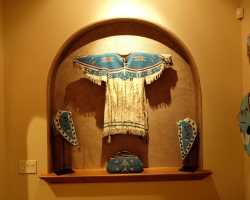 Beadwork: Woman's beaded shirt, pair of tapaderos, beaded bag. To the side a beaded vest and a pair of beaded gauntlets.